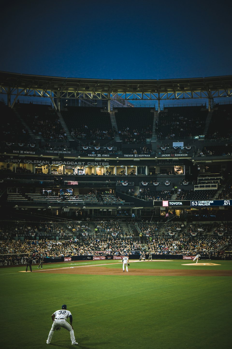 Night baseball game with players on the field and a large crowd in the stands.