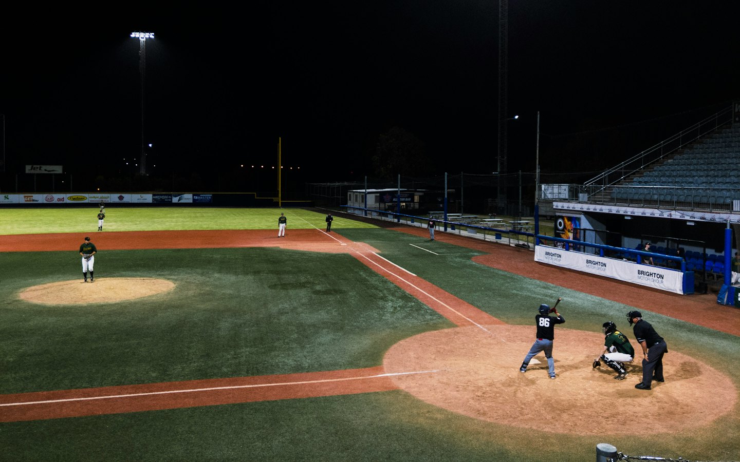 Baseball players bat, pitch, and catch during a night game.