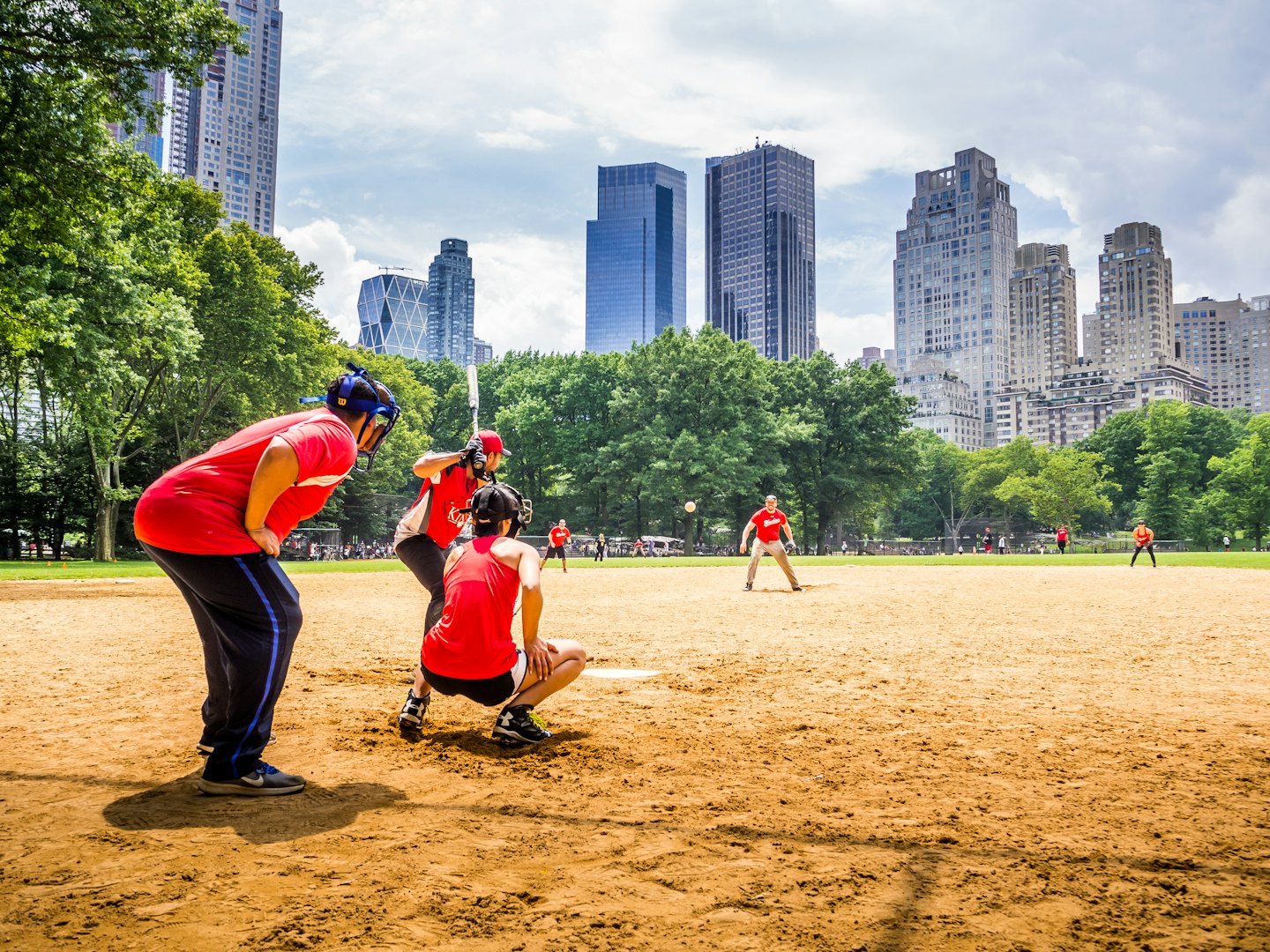 Players enjoying a sunny baseball game in a city park.